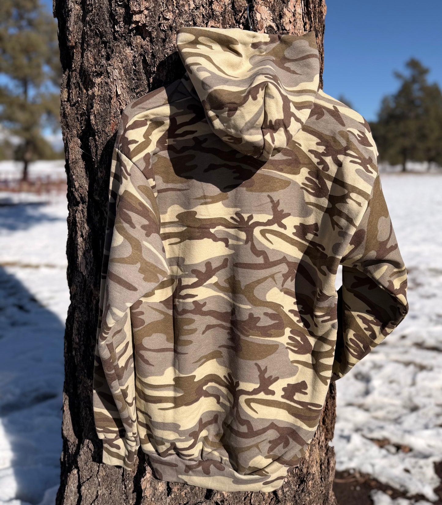 Back of the camouflage hoodie hanging on a tree with a blurred forest background