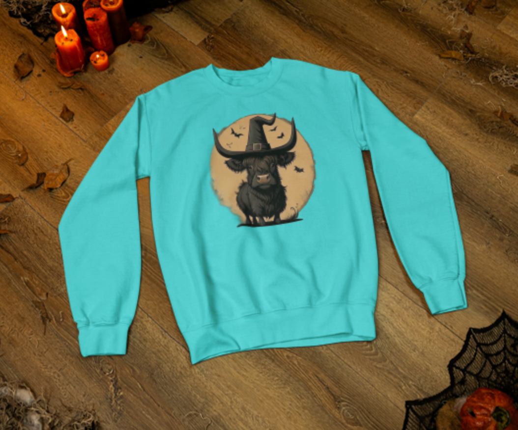 Light blue sweatshirt with a graphic design of a bull wearing a witch hat on a wooden surface.
