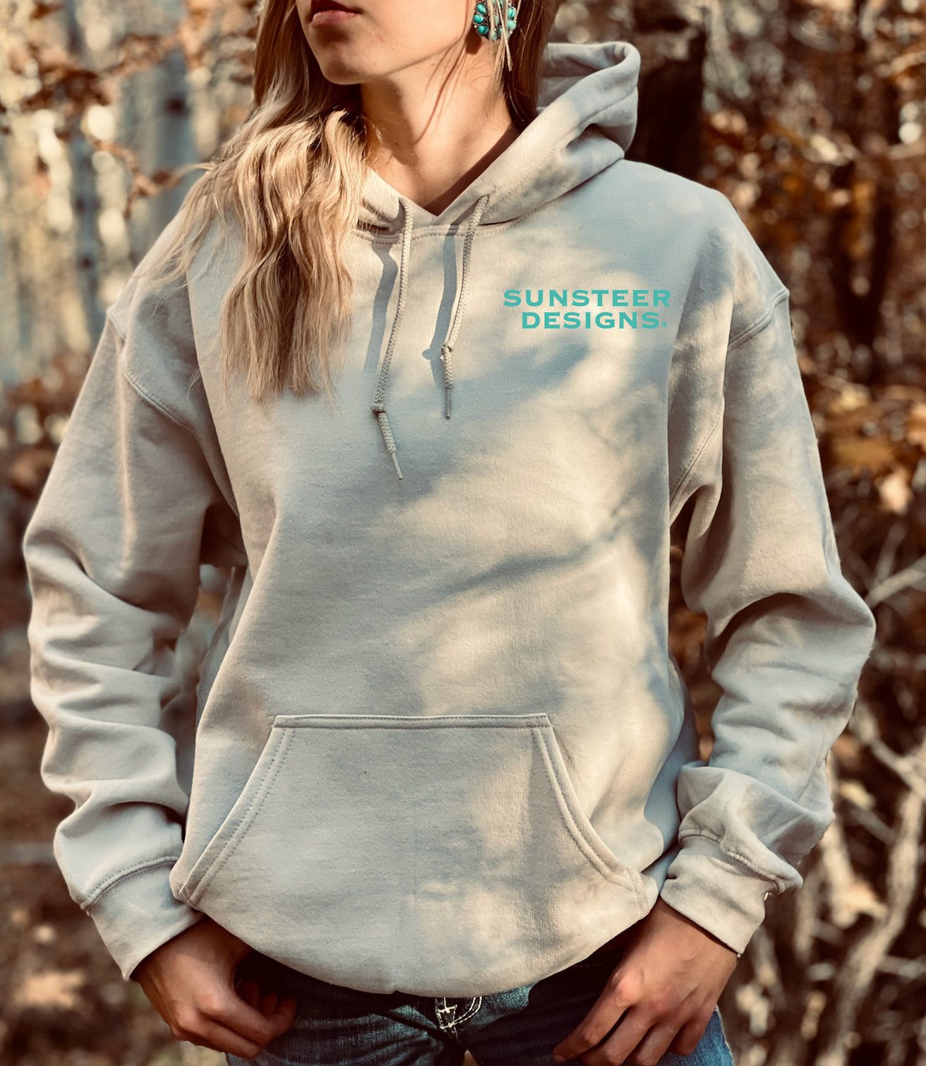 Person wearing a tan hoodie with 'Sunsteer Designs' logo outdoors.