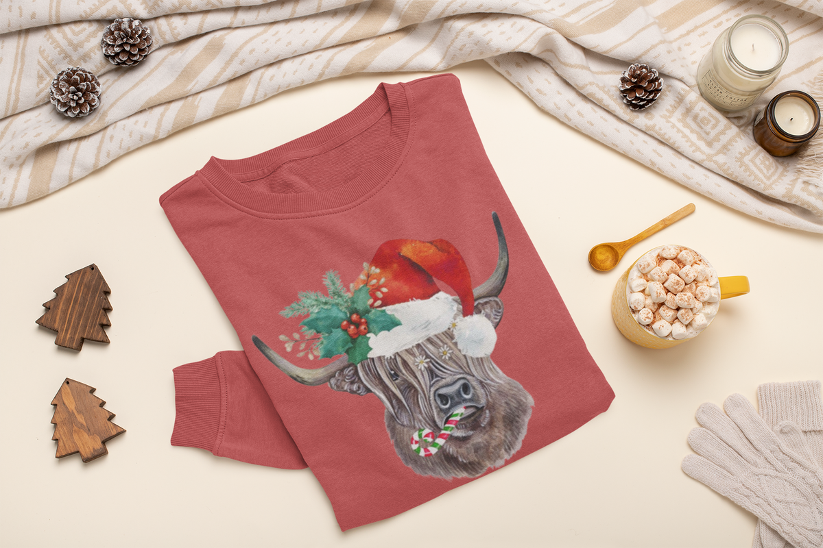 Red sweatshirt with a highland cow wearing a Santa hat on a beige surface with holiday decorations.