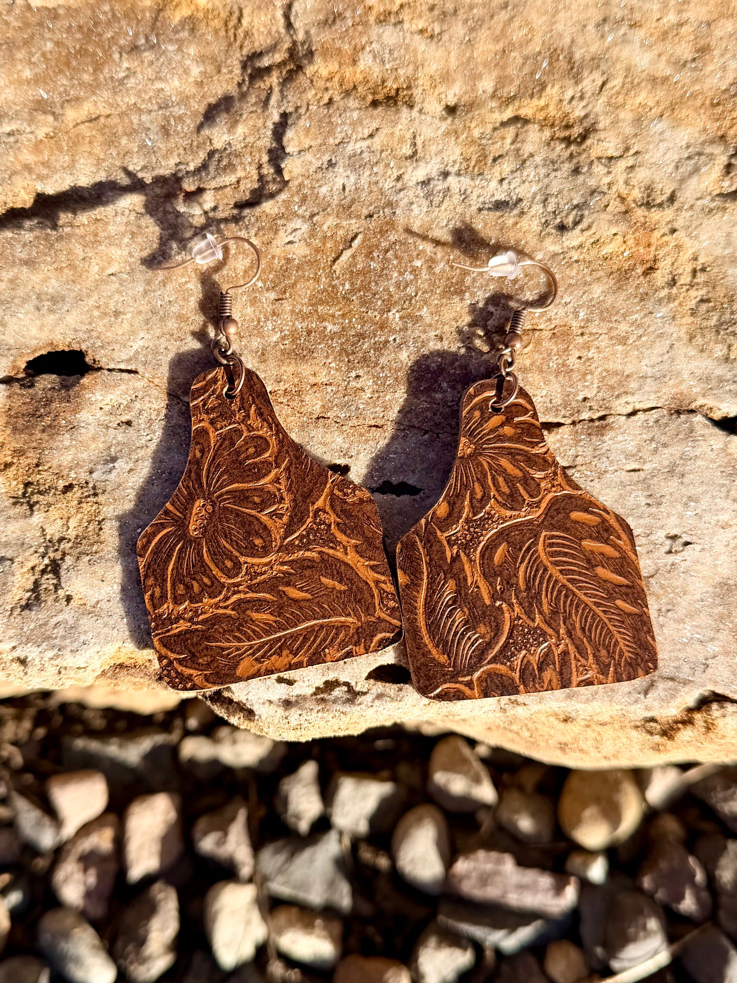 Brown leather earrings with embossed patterns on a stone surface
