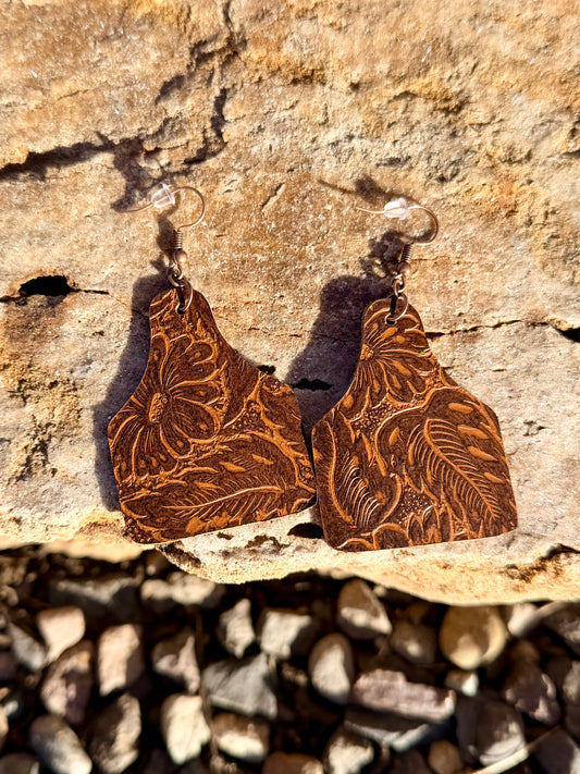 Brown leather earrings with embossed patterns on a stone surface
