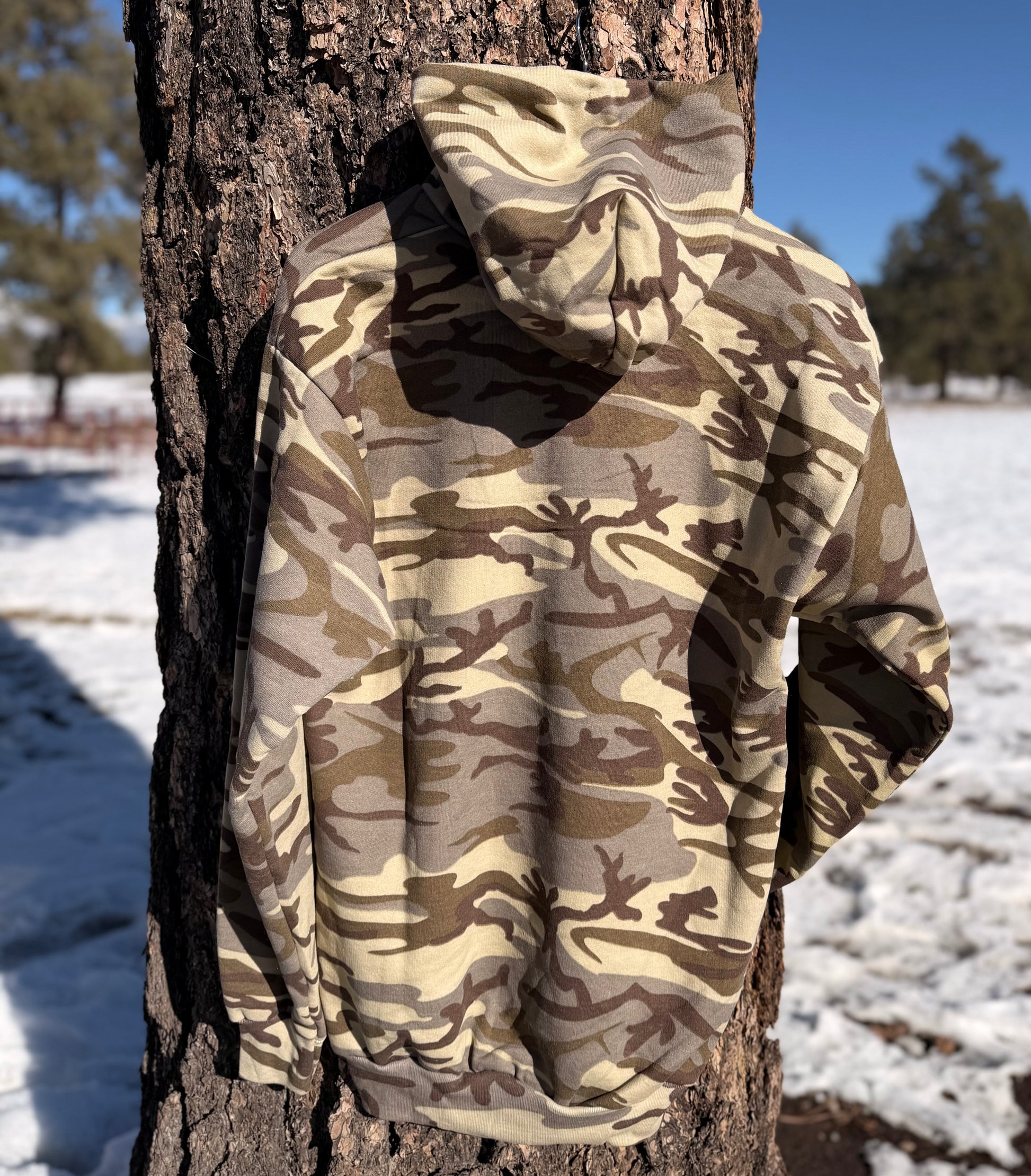 Back of the camouflage hoodie hanging on a tree with a blurred forest background