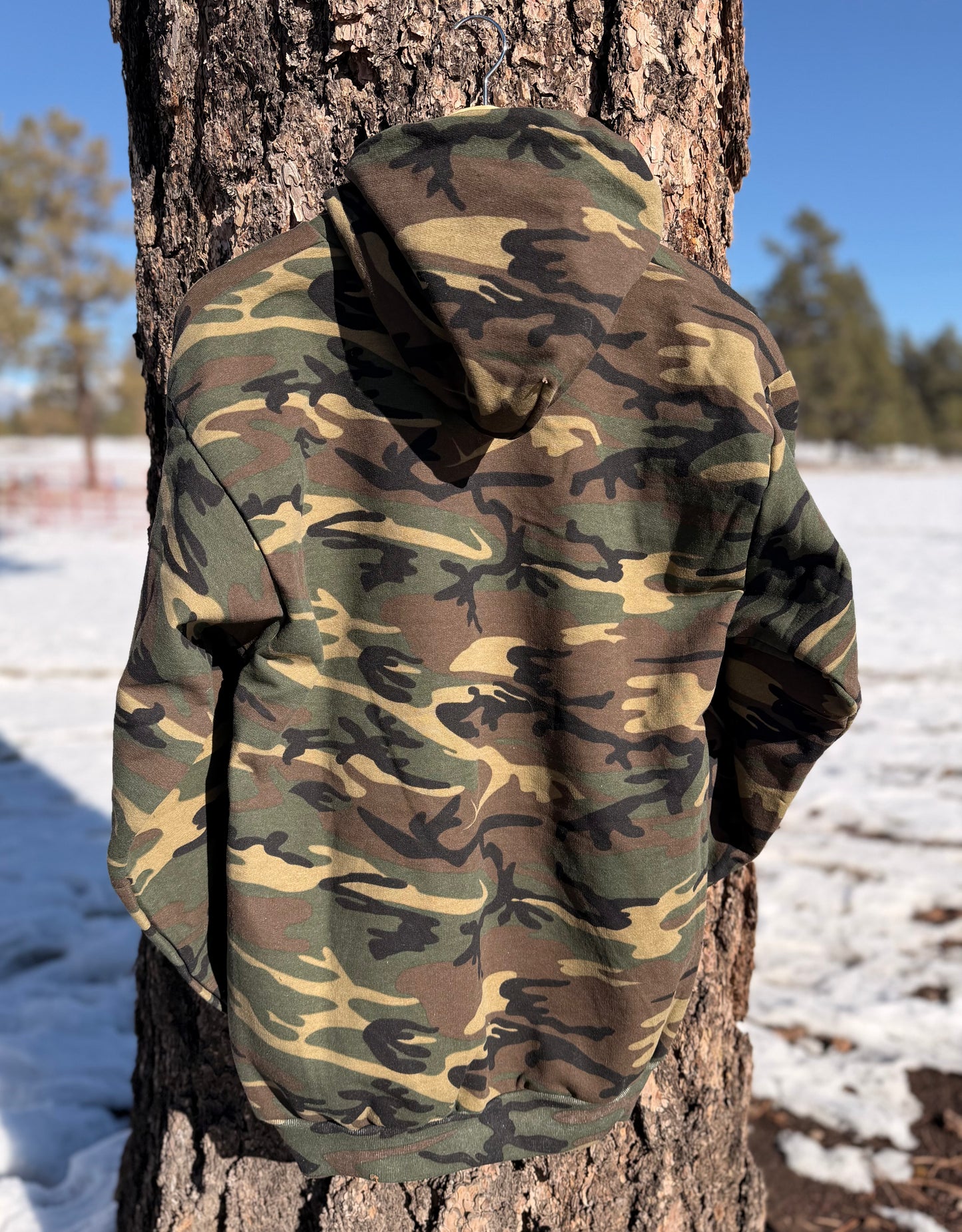 Camouflage-patterned hoodie hanging on  a tree in a snowy landscape