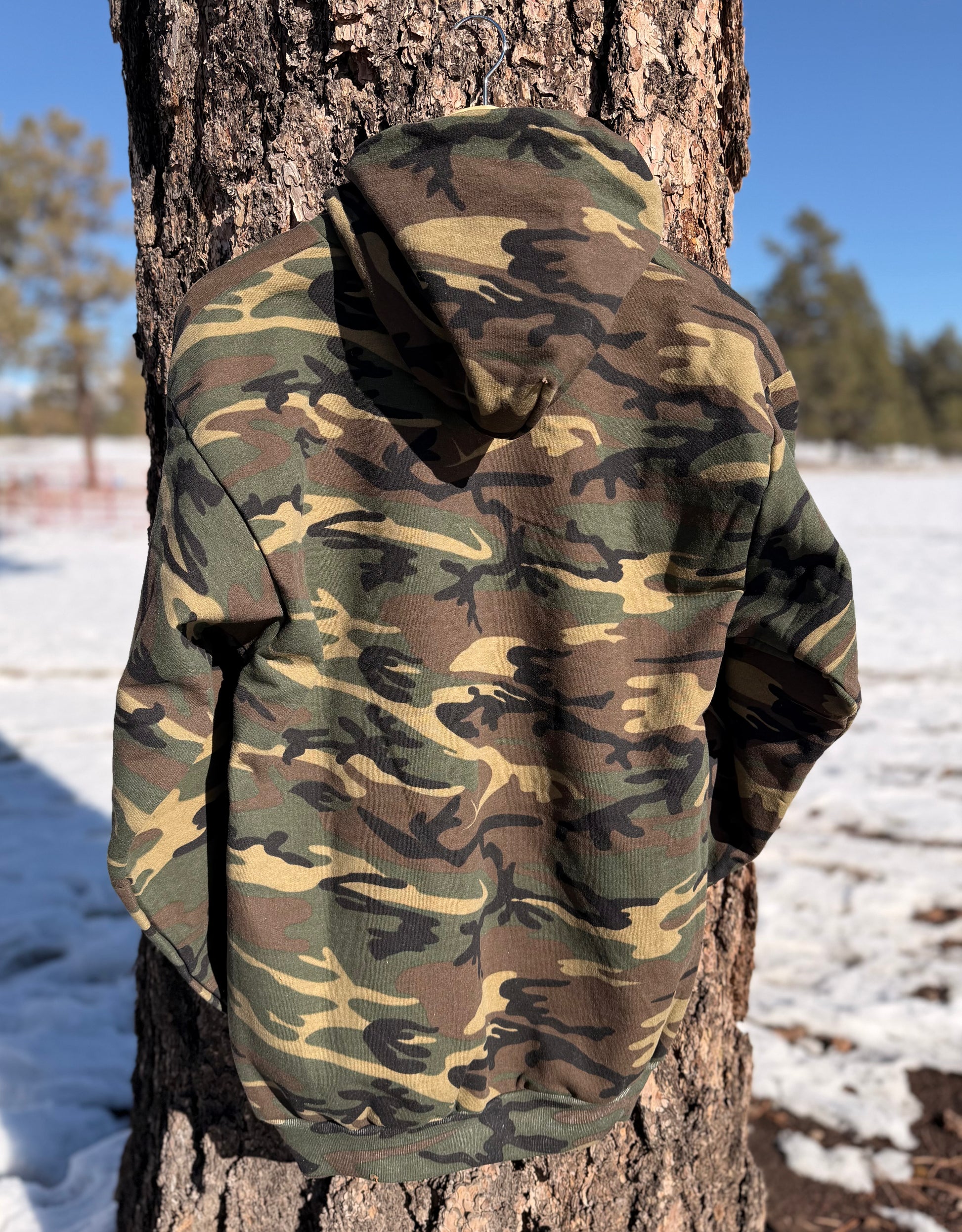 Camouflage-patterned hoodie hanging on  a tree in a snowy landscape