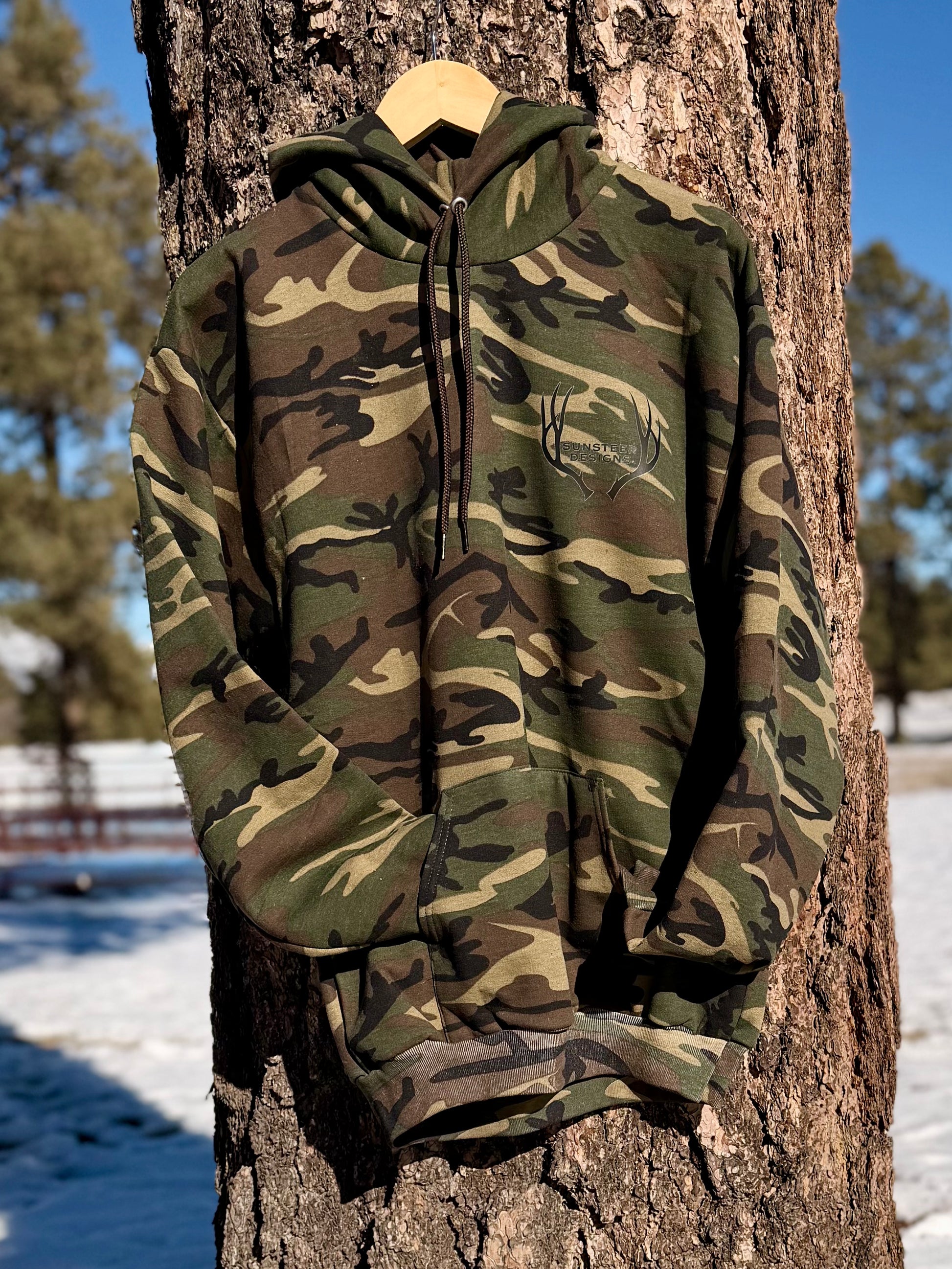 Camouflage hoodie hanging on a tree branch with a snowy landscape in the background