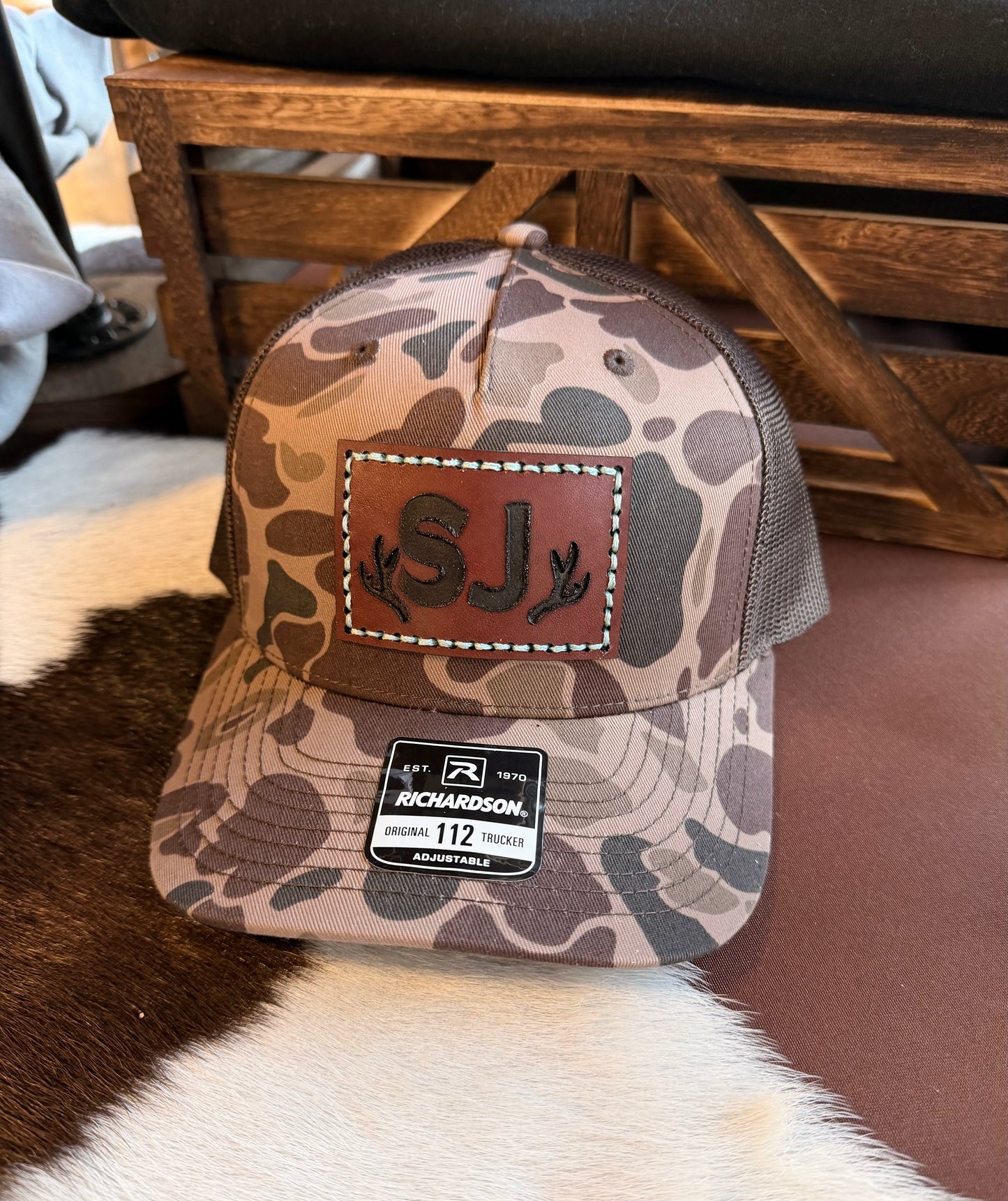 Brown Duck Camouflage baseball cap with custom branded leather patch and Richardson logo with a wooden background.