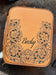 A tan leather zippered case with floral cutout detailing and the name 'Becky' printed on the front, placed on a cowhide surface.