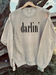 Sandstone tan sweatshirt with black 'darlin' text on a wooden hanger against a natural background