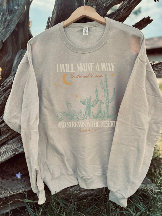 Beige sweatshirt with desert-themed design and 'I will make a way in the desert' verse text on a wooden surface