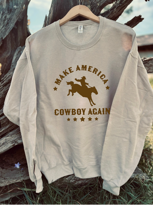 Sandstone sweatshirt with brown 'Make America Cowboy Again' text and graphic on a wooden surface.
