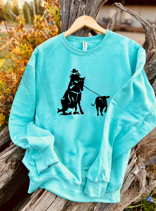 Mint sweatshirt with black graphic of a person riding a horse and roping a breakaway calf, on a hanger against a natural background.