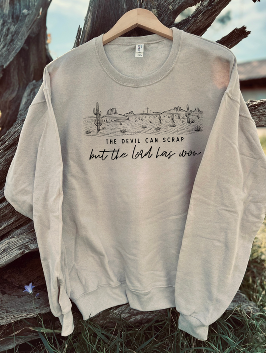 Sandstone sweatshirt with 'the devil can scrap but the lord has won' text with a dessert scene on a wooden surface