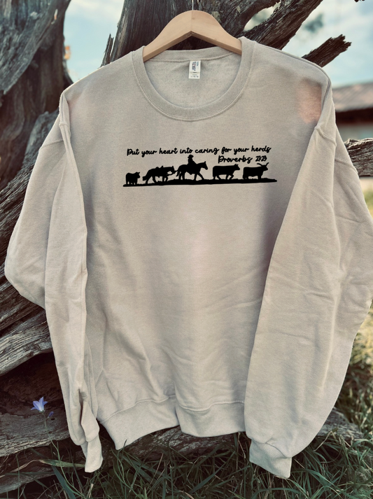 Tan sweatshirt with a proverbs 27:23 verse and cowboy graphic design on a wooden background