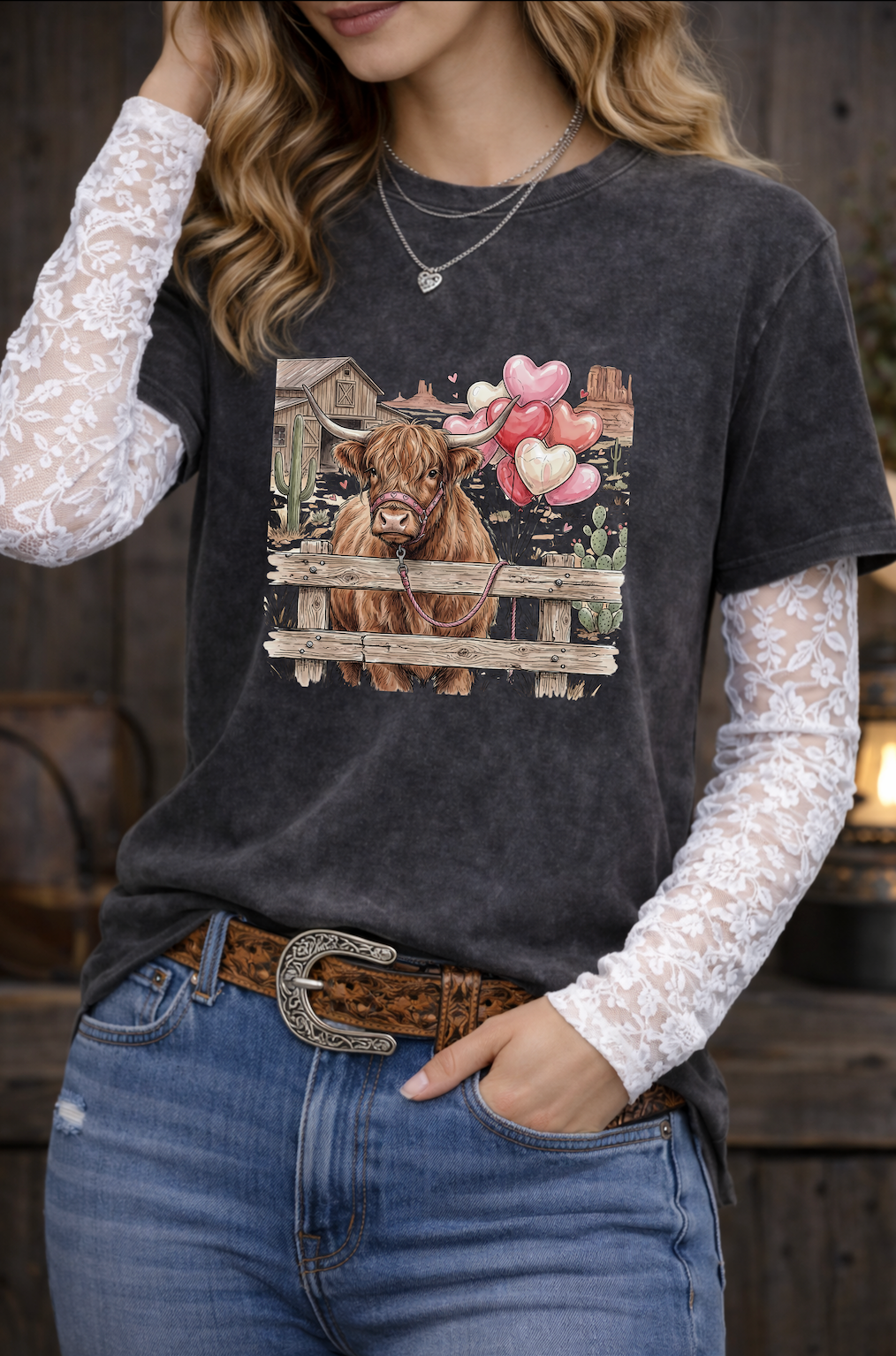 Person wearing a black t-shirt with a cow graphic, white lace sleeves, and blue jeans.
