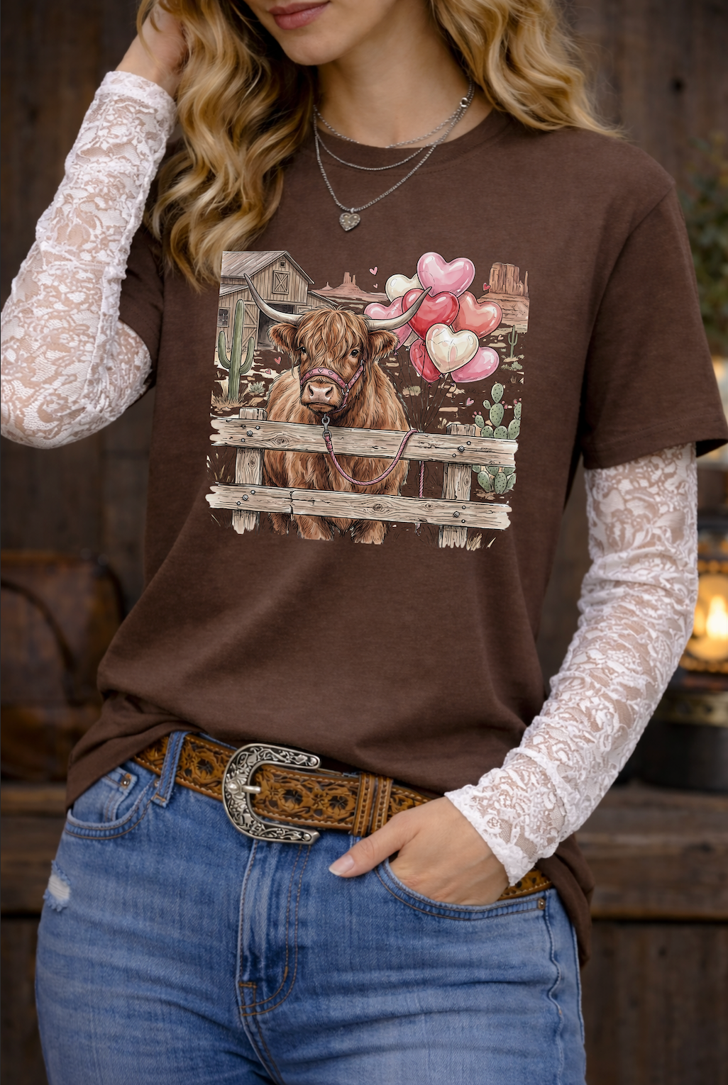 Woman wearing a brown t-shirt with a cow graphic, white lace sleeves, and blue jeans.