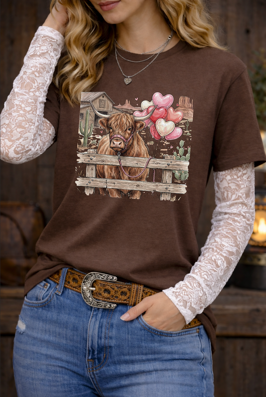 Woman wearing a brown t-shirt with a cow graphic, white lace sleeves, and blue jeans.