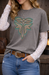 Person wearing a gray t-shirt with a leaf design, white lace sleeves, blue jeans, and a brown belt.