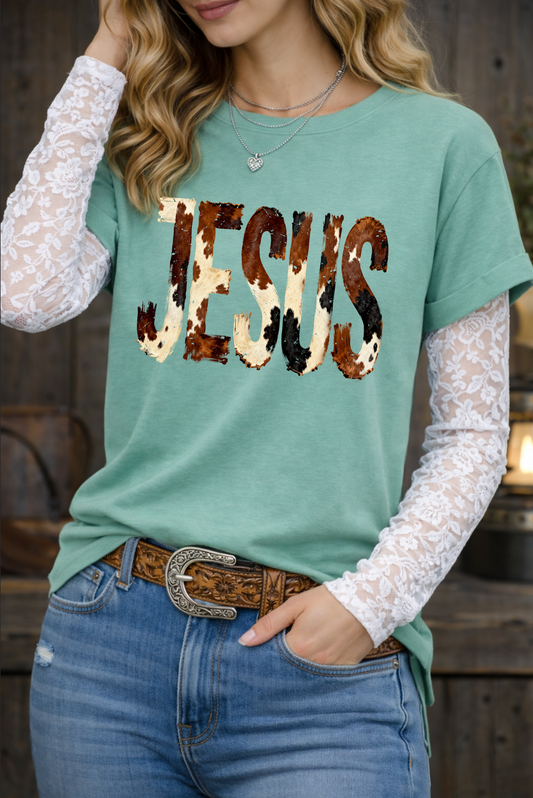 Person wearing a green t-shirt with 'JESUS' printed in leopard print, lace sleeves, and jeans.