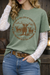 Person wearing a green t-shirt with a graphic design, white lace sleeves, and blue jeans.